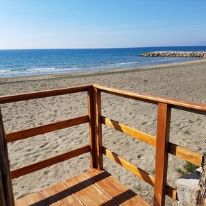 Une terrasse en bois mène à une plage de sable, avec une côte rocheuse en arrière-plan.
