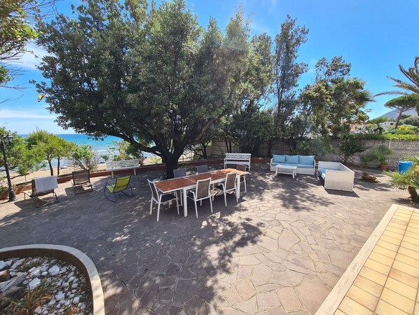 Une terrasse extérieure avec une table et des chaises, un canapé et un banc, le tout donnant sur une plage.