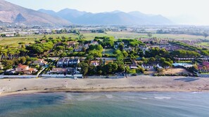 An aerial view of a coastal town with houses, a beach, and mountains in the background.