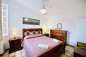 A hotel room with a bed, a nightstand, a dresser, a mirror, and a ceiling fan.