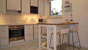 Ett modernt kök med vita skåp, en inbyggd ugn, en mikrovågsugn och en liten bardisk med barstolar.
