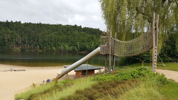 A beach with a rope bridge and a slide leading to a wooden cabin. - Cozy tent roof house for up to 6 people, free WLAN, pet-friendly (Bad Arolsen)
