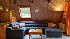 A cozy room with a sectional sofa, a wooden coffee table, and a window with a view of greenery.