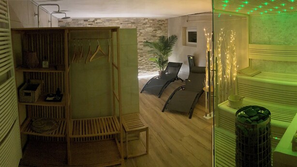 Een kamer met een houten bankje, een klein tafeltje, een hangrek en een pot met een plant.