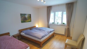 Een slaapkamer met twee bedden, een stoel, een raam met gordijnen, een radiator en een schilderij aan de muur.