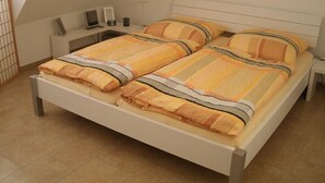 Un lit double avec une couvre-lit à rayures et des oreillers, une table de chevet avec une lampe, et un petit bureau avec un ordinateur et un cadre photo.