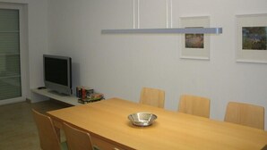 Un coin repas avec une table en bois, quatre chaises, un saladier en argent, un téléviseur à écran plat et des tableaux encadrés accrochés au mur.