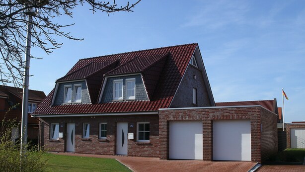 Une maison à deux étages, avec un toit recouvert de tuiles rouges, une façade en briques et deux portes de garage.
