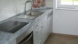 Une cuisine avec des meubles gris, un évier en acier inoxydable, un four encastré et une fenêtre donnant sur un paysage verdoyant.