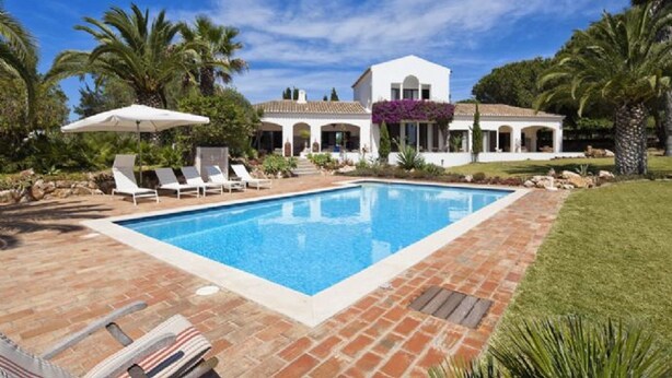 Une piscine avec des chaises longues et, en arrière-plan, un bâtiment blanc orné d’arches.
