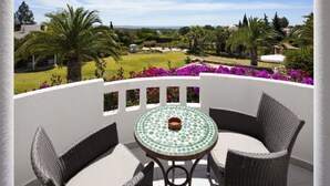 Un balcon agrémenté d’une table ronde et de chaises en osier, donnant sur un jardin aménagé avec des palmiers et des fleurs violettes.