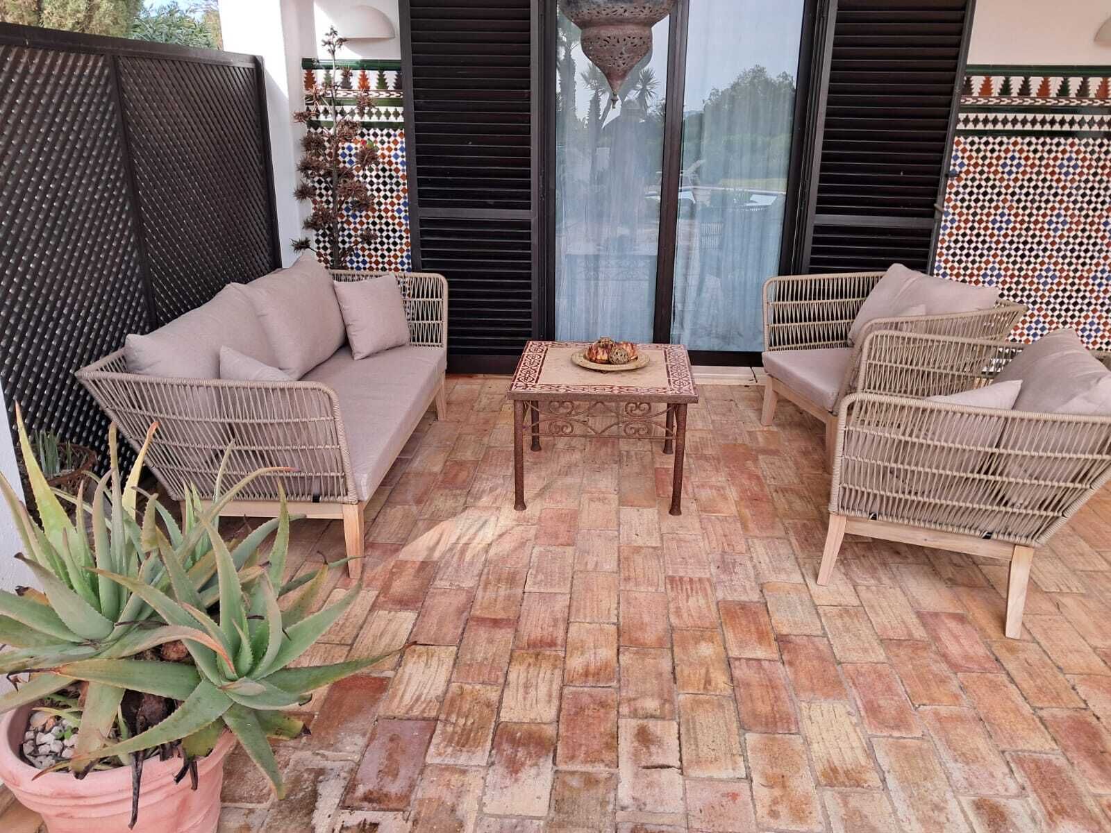 A patio with wicker furniture, a small table, and a potted plant.