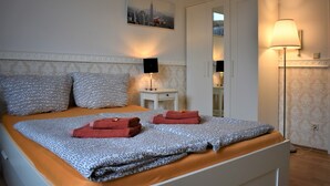 A neatly made bed with patterned bedding, a bedside lamp, and a cityscape painting on the wall. - Great price in the old town and center, nice view, central, cozy with heart (Heidelberg)