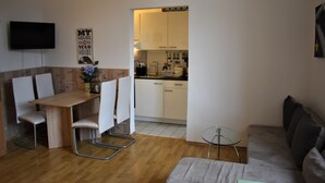 A modern living room with a wooden dining table, white chairs, a grey sofa, and a small glass table. A kitchen is visible through an open doorway. - Great price in the old town and center, nice view, central, cozy with heart (Heidelberg)
