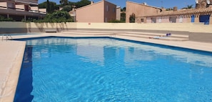 Una piscina rettangolare con acqua cristallina, circondata da un solarium color beige e un muretto basso.