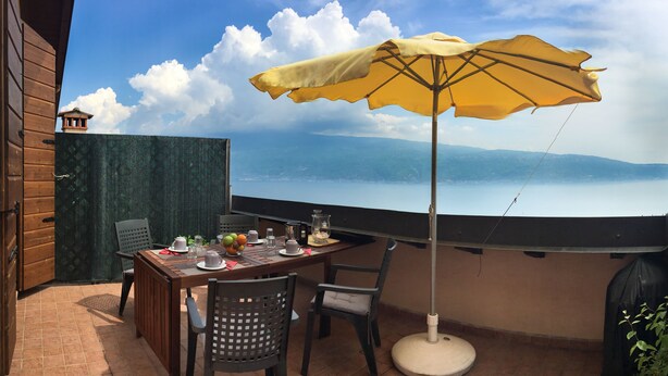 Een terras met een tafel voor twee personen, een gele parasol en uitzicht op een meer.