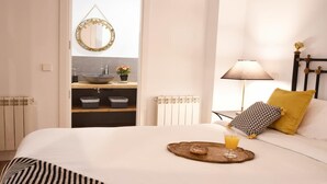 A hotel room with a bed, a bedside table with a lamp, a breakfast tray with toast and juice, a bathroom with a sink and mirror, and a radiator. - DIWAN Suite apart. 4BDR / 5BTH - Atocha / City Center (Madrid)