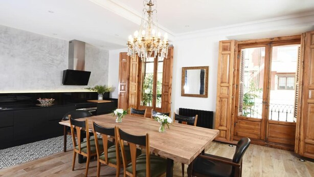 A modern kitchen with a wooden dining table, chairs, and a chandelier. - DIWAN Suite apart. 4BDR / 5BTH - Atocha / City Center (Madrid)