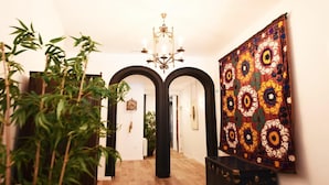 A hallway with a large painting, a chandelier, and bamboo plants. - DIWAN Suite apart. 4BDR / 5BTH - Atocha / City Center (Madrid)