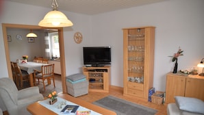 A living room with a TV, wooden cabinet with glassware, and a dining area with chairs and a table. - Vacation home Lilli 35610 - Holiday home Lilli (Uplengen)
