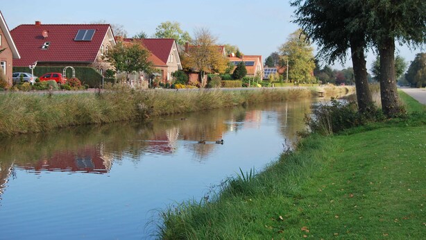 A calm river with houses on one side and a grassy bank on the other. - Vacation home Lilli 35610 - Holiday home Lilli (Uplengen)