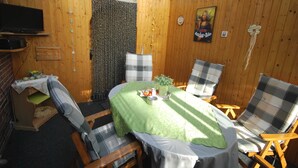 A wooden-paneled room with a table covered by a green tablecloth, two plaid chairs, a television on a shelf, and a door with a patterned curtain. - Vacation home Lilli 35610 - Holiday home Lilli (Uplengen)