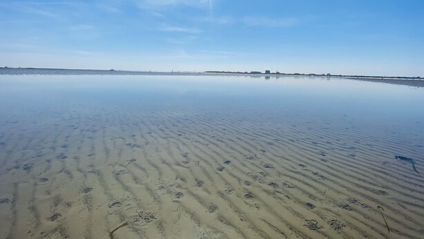 A wide, calm beach with clear skies and a visible jet trail.