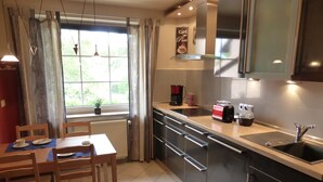 A modern kitchen with a dining area, featuring a window with curtains, a coffee maker, a toaster, and a sink.