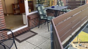 A patio area with a table and chairs, a wooden bench, and a glass door leading to an indoor space.