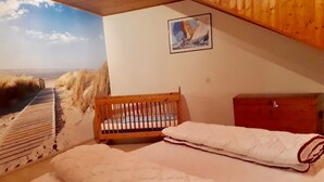 A bedroom with a bunk bed, a wooden crib, a wooden dresser, and a beach mural on the wall.