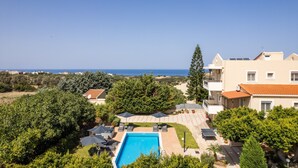 Un espace piscine offrant une vue dégagée sur la mer, entouré d’arbres et de bâtiments.