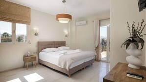 Une chambre à coucher avec un lit, des tables de chevet, un luminaire suspendu, une plante en pot et une vue sur l’extérieur.