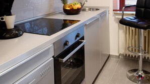 A modern kitchen with stainless steel appliances, a bowl of fruit on the counter, and a bar stool near the window. - 2-room apartment for 1 - 4 people (Bergisch Gladbach)
