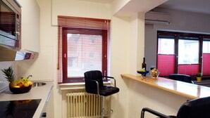 A kitchen with a fruit bowl, a bar stool, and a window with blinds. - 2-room apartment for 1 - 4 people (Bergisch Gladbach)