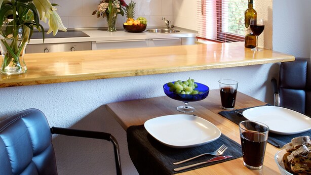 A modern kitchen with white cabinets, a microwave, and a dining area with a table, chairs, and a vase of flowers. - 2-room apartment for 1 - 4 people (Bergisch Gladbach)
