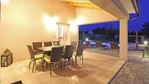 An outdoor patio area with a dining table and chairs, a lantern, and a view of a swimming pool at dusk.