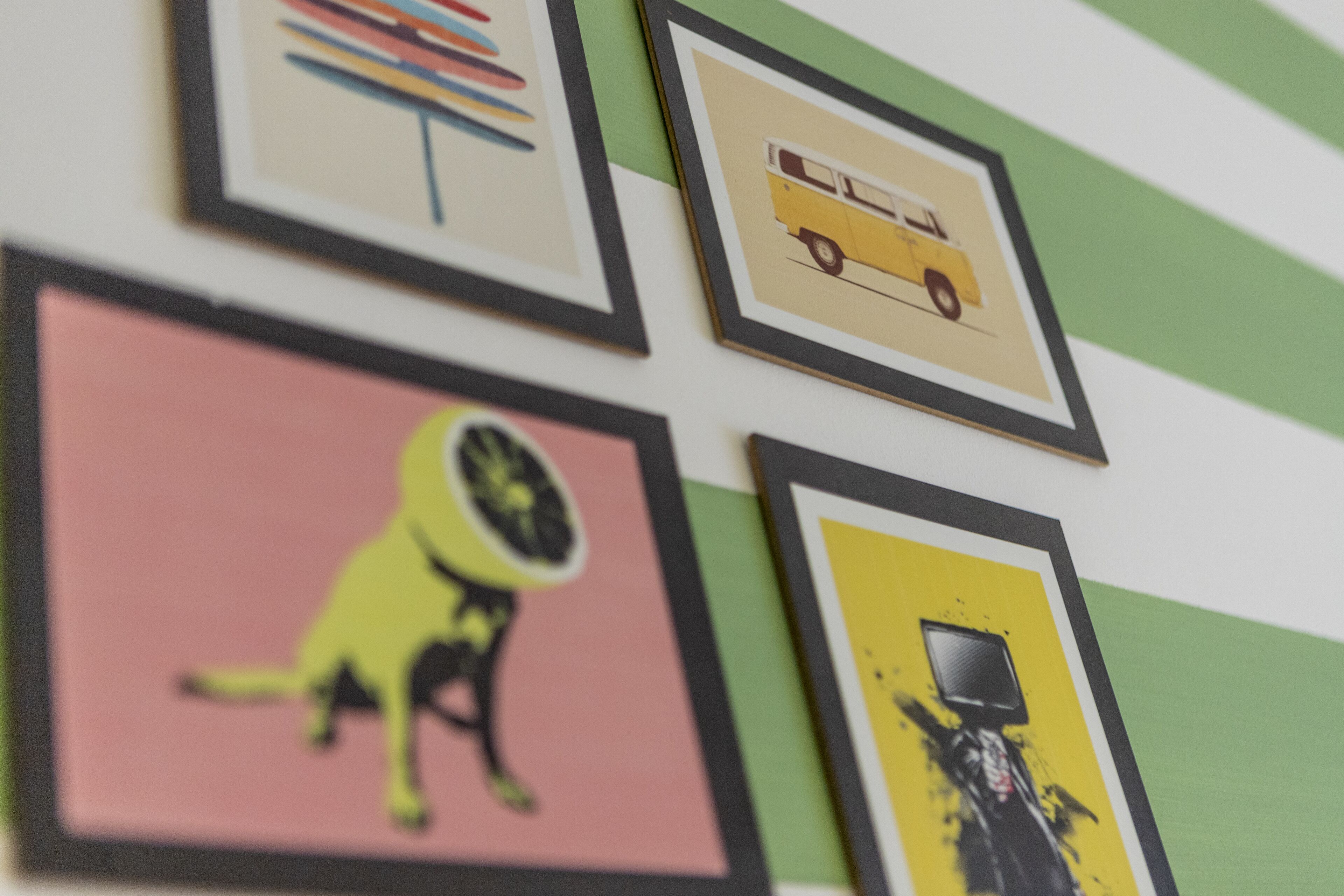 A wall with framed pictures including a yellow bus, a dog, and abstract art.