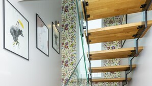 A modern staircase with wooden steps and glass railings, leading to a landing with a floral-patterned wall.