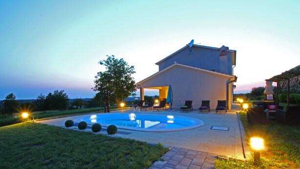 A modern house with a swimming pool, outdoor seating, and a well-lit patio area.