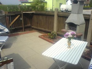 Une terrasse avec une table, des chaises, une clôture en bois et un barbecue.
