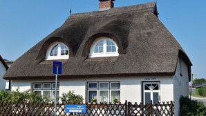 Een traditioneel gebouw met rieten dak, twee gebogen ramen en een bord dat een bedrijf aanduidt.
