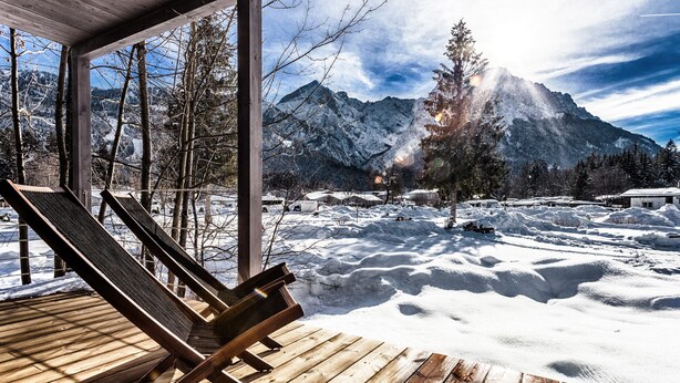 A wooden deck with a lounge chair, a mountain view, and snow-covered ground. - Zugspitz-Rauschen 1 - Live like a dream right on the riverbank with a view of the Zugspitze (Garmisch-Partenkirchen)