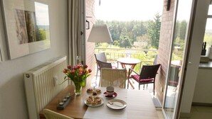 A dining area with a table set for two, a vase with flowers, and a view of a garden through a glass door. - 2 room apartment 36 sqm for 2 guests Swimming pool and sauna approx. 8 minutes walk to the beach WLAN (Zinnowitz)