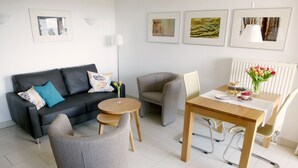 A modern living room with a sofa, two armchairs, a wooden coffee table, a dining table with chairs, and artwork on the walls. - 2 room apartment 36 sqm for 2 guests Swimming pool and sauna approx. 8 minutes walk to the beach WLAN (Zinnowitz)