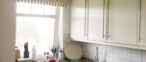 A kitchen with white cabinets, a stainless steel sink, and a window with striped valance.