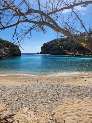 A beach with clear turquoise water, pebbly shore, and rocky cliffs. - Romantic villa,quiet location, private pool, sun terrace, 10 min. to the beach! (Ag. Ioannis)