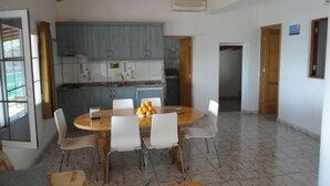 A dining area with a round table, white chairs, and a fruit bowl. There is a kitchen in the background with blue cabinets and a window. - Rural House of Perera with private pool for 4 people (San Bartolomé de Tirajana)
