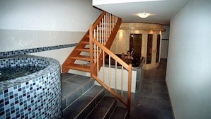 A spa area with a wooden staircase, a hot tub, and a tiled wall. - Newly built comfortable apartment with wellness area  (Jachenau)