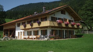 A two-story building with a sloped roof, multiple windows, and flower boxes on the balcony. - Newly built comfortable apartment with wellness area  (Jachenau)