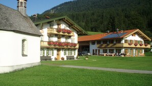 A traditional Alpine-style building with a sloped roof, a bell tower, and a balcony with flower boxes. - Newly built comfortable apartment with wellness area  (Jachenau)